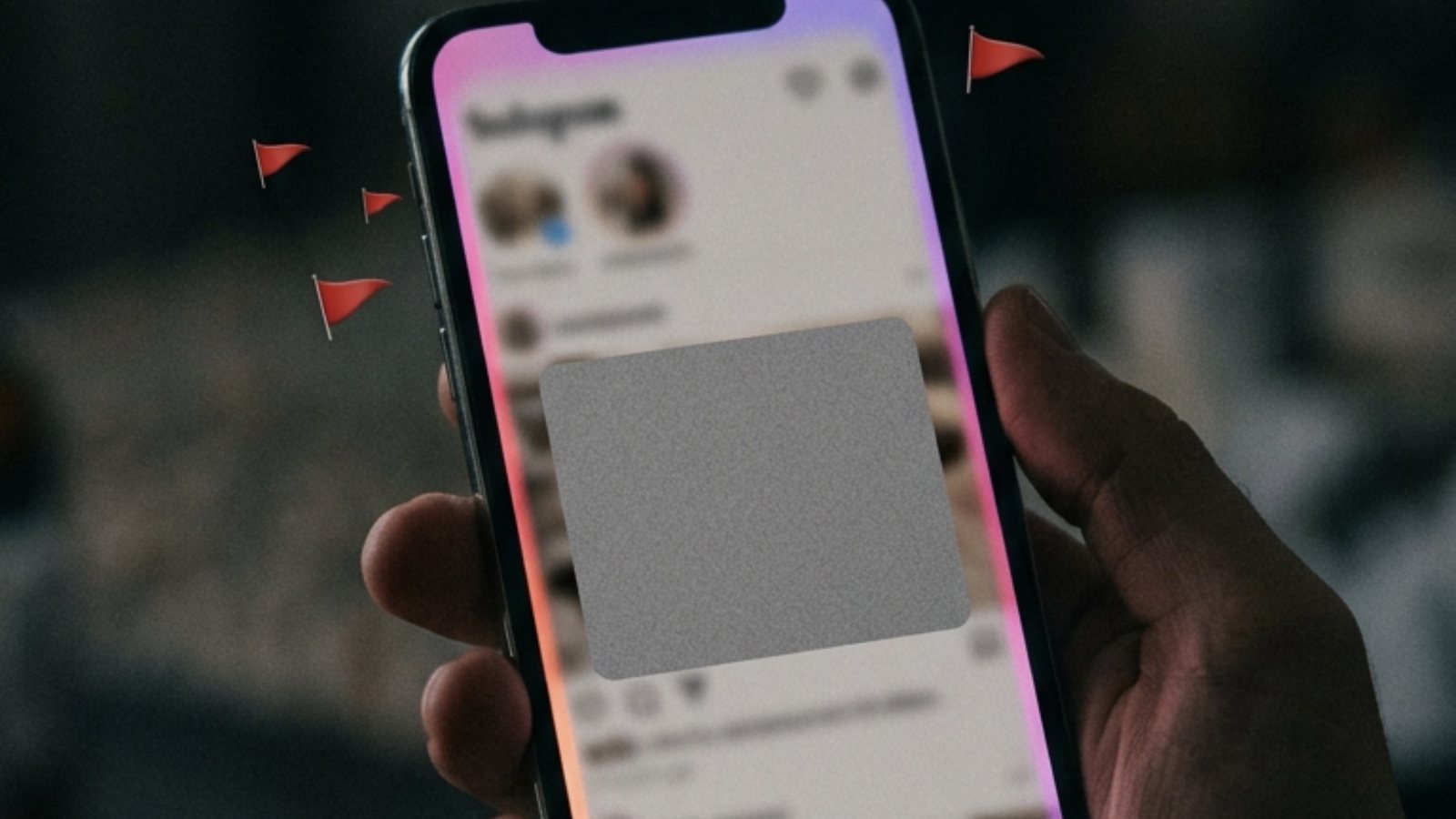 Mão segurando um celular com o feed de uma rede social de bordas em rosa e roxo, um painel cinza cobrindo a publicação e bandeirinhas vermelhas de denúncia flutuando ao redor